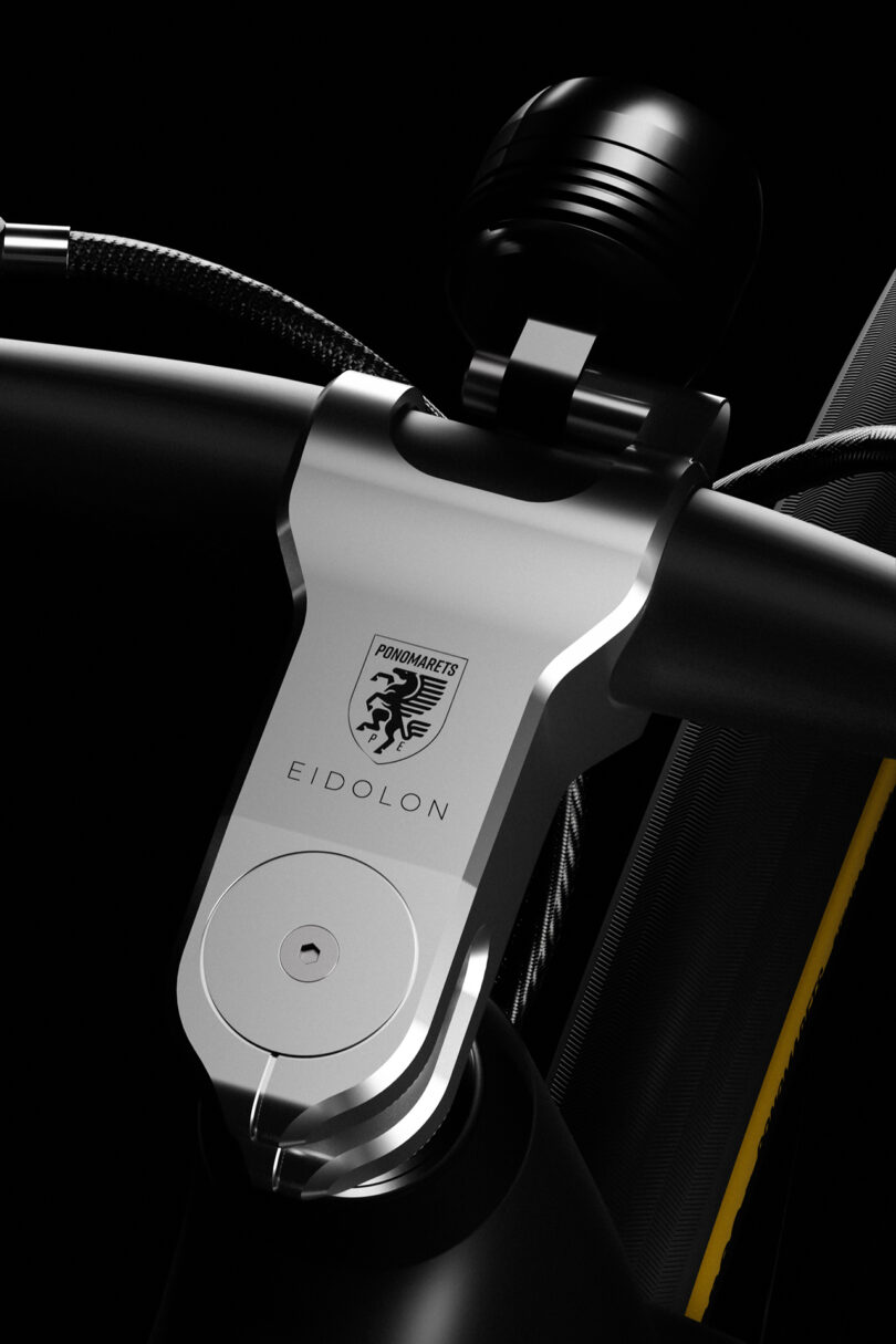 Close-up of a sleek bicycle handlebar stem with "Eidolon" and logo engraving. Features modern design elements in silver and black with attached gear shift.